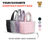 Four nappy bags in black, gray, purple, and pink on a beige background with text about a money-back guarantee.